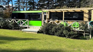 A green bus parked in a grassy area with a wooden structure nearby. - Escape to Tranquillity: The Bus Stop Your Tiny Home Bus Retreat (Wainuiomata Coast)