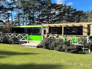 A green bus parked in a grassy area with a wooden structure nearby.