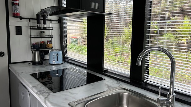 A modern kitchen with a stainless steel sink, black cabinets, and a marble countertop. - Escape to Tranquillity: The Bus Stop Your Tiny Home Bus Retreat (Wainuiomata Coast)