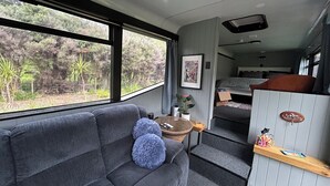 A cozy interior with a sofa, a small table, and a bunk bed. - Escape to Tranquillity: The Bus Stop Your Tiny Home Bus Retreat (Wainuiomata Coast)