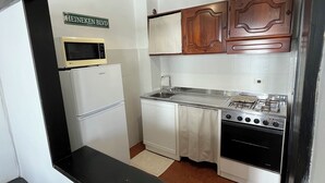 Una cocina compacta con armarios blancos, estufa, microondas y una lámpara colgante.