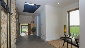 A spacious interior with a large window offering a view of a green field. - Tithe Barn Lodge (Bodorgan)