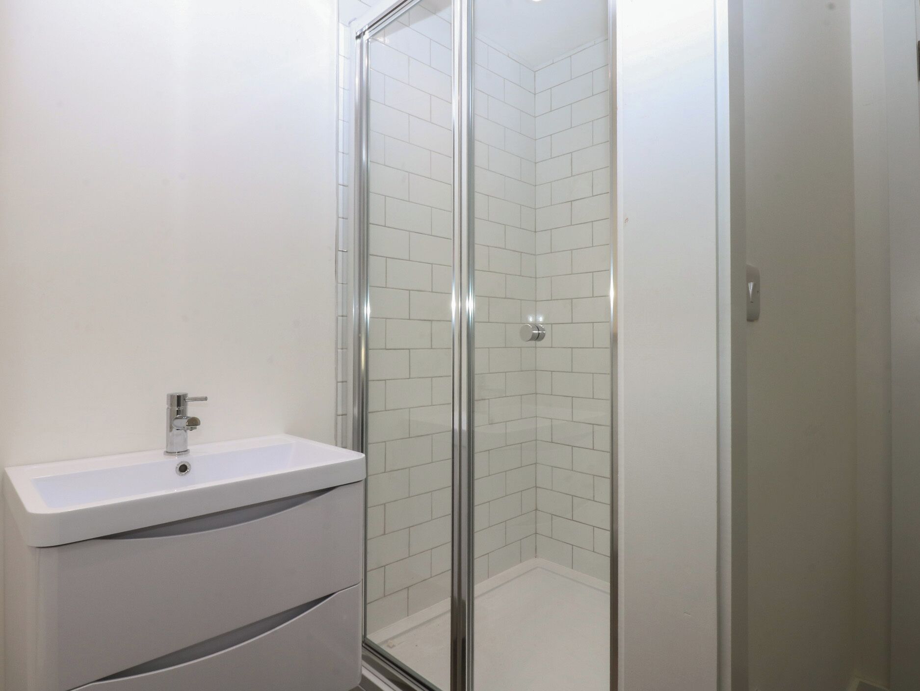 Een badkamer met een douchecabine van glas, een witte wastafel en een spiegel.