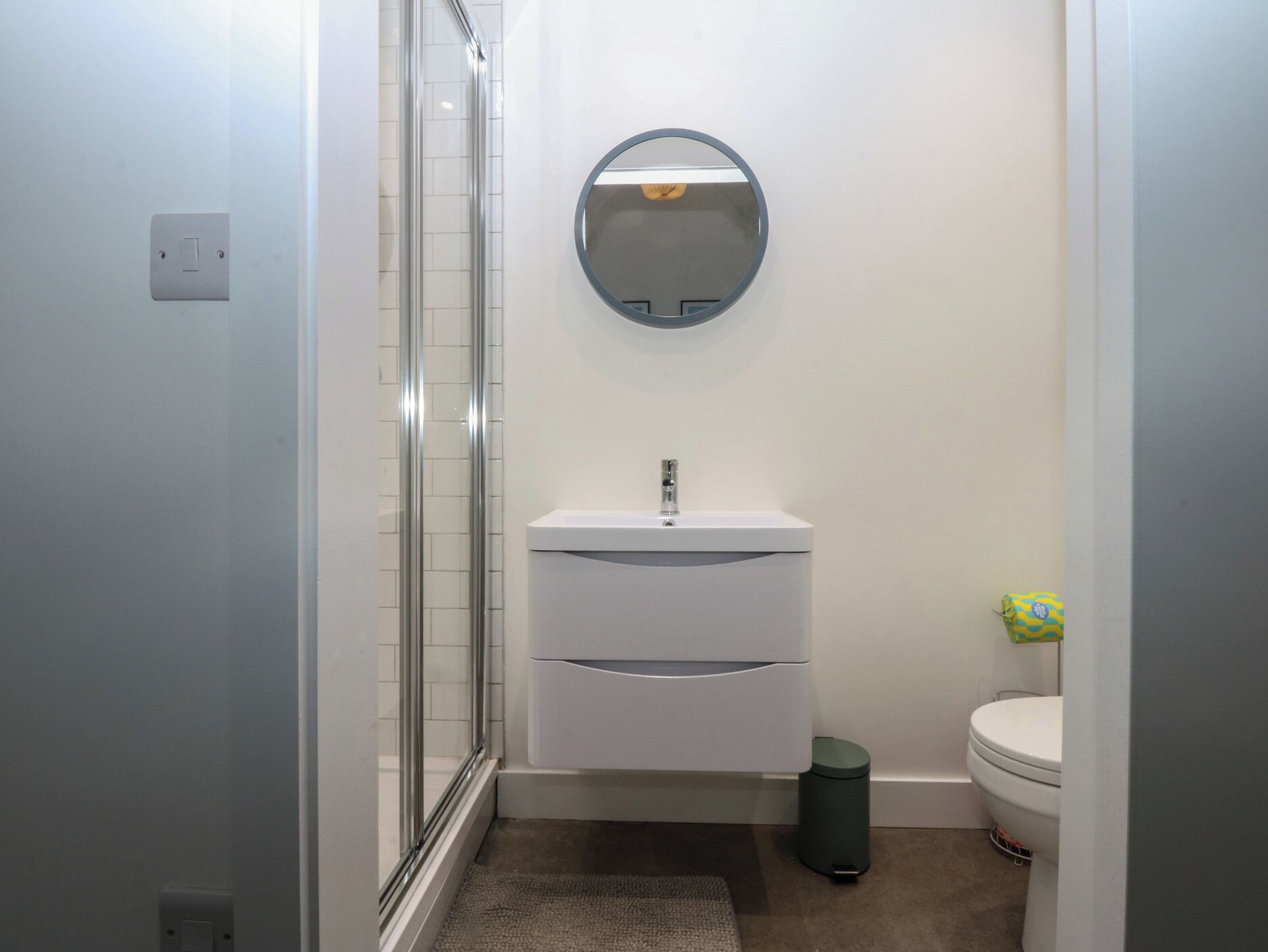 Un baño pequeño y moderno con cabina de ducha de vidrio, un lavamanos blanco con espejo arriba y un inodoro.