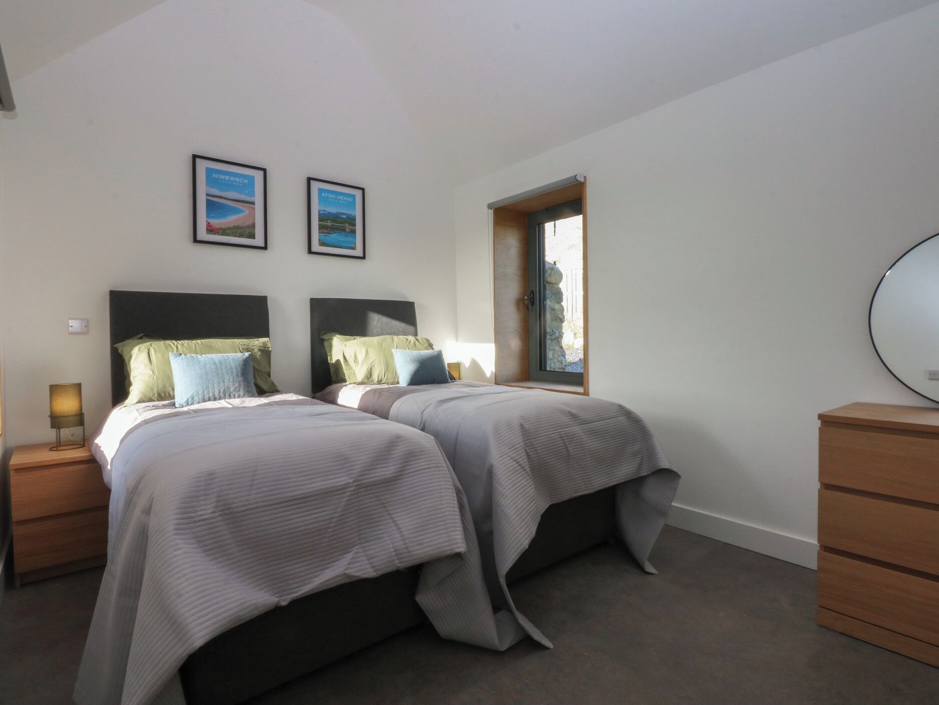 A bedroom with two beds, a dresser, a nightstand, a lamp, and a window with a view.