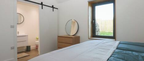 A bedroom with a bed, a dresser, a mirror, a window, and a bathroom with a sink and toilet.