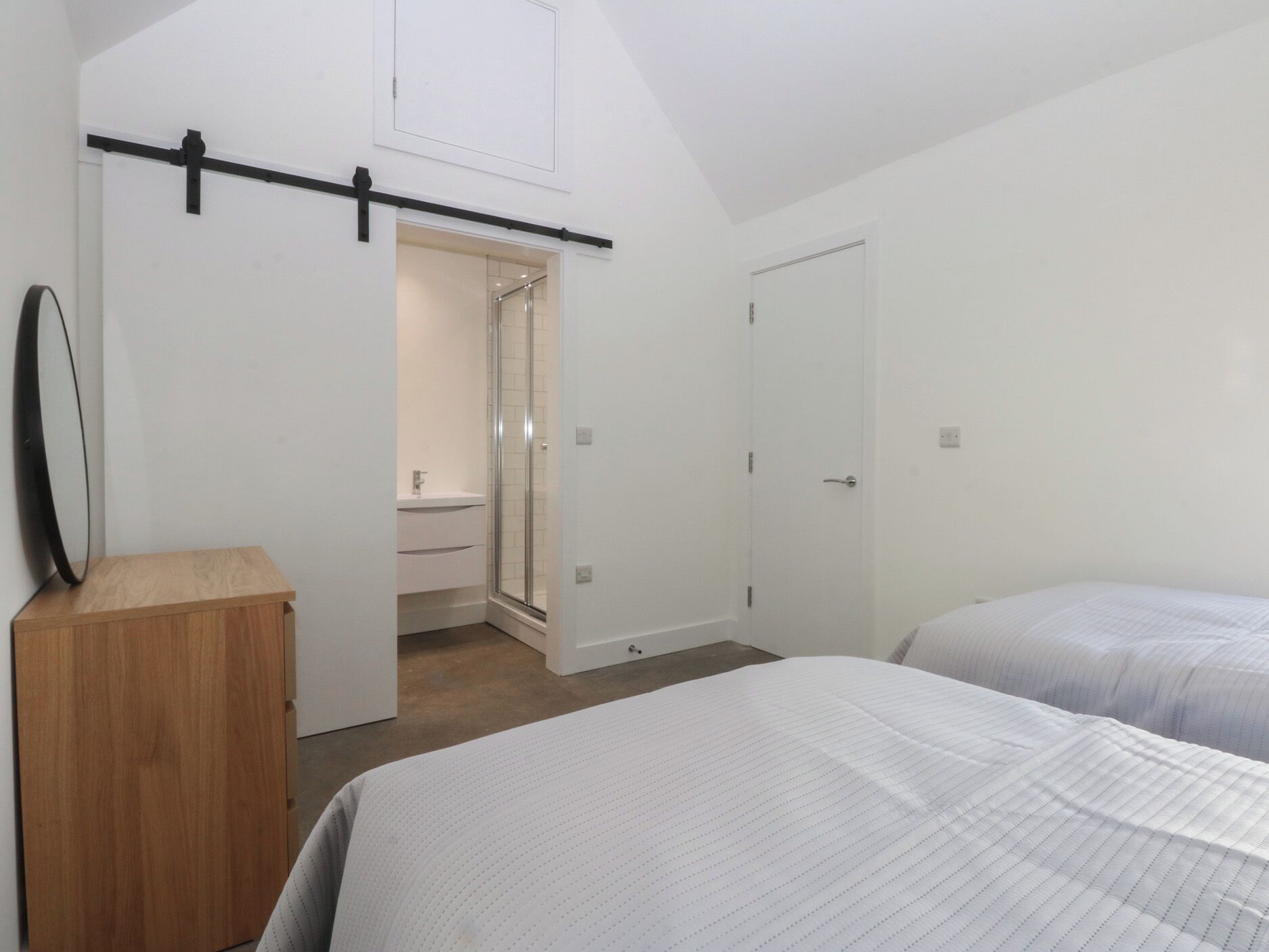 Une chambre à coucher avec un lit, une commode en bois, une porte et une salle de bain avec une douche.
