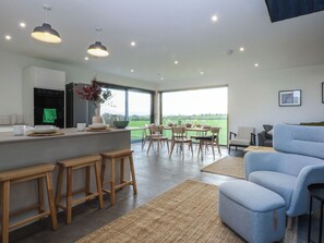 A modern kitchen with a large island, wooden stools, and a dining area with a view of the countryside. - Tithe Barn Lodge (Bodorgan)