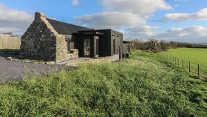 A stone cottage with a modern extension, surrounded by a grassy field and a wooden fence. - Tithe Barn Lodge (Bodorgan)