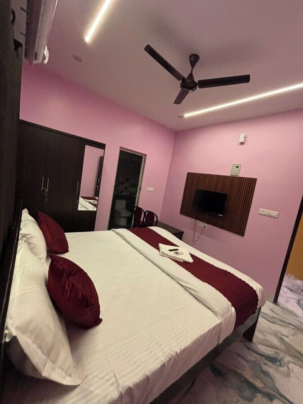 Une chambre à coucher avec un lit, un ventilateur de plafond, un téléviseur fixé au mur et un miroir.