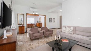 A modern living room with a flat-screen TV, two armchairs, a sofa, a glass coffee table, and a dining area in the background. - Casa Centrale by Nomads (Paphos)