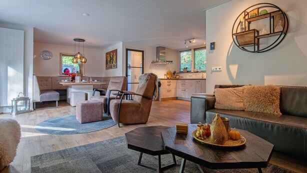 A modern living room with a sofa, a coffee table, and a dining area with a table and chairs. - Lovely villa on the edge of the forest (Den Burg)