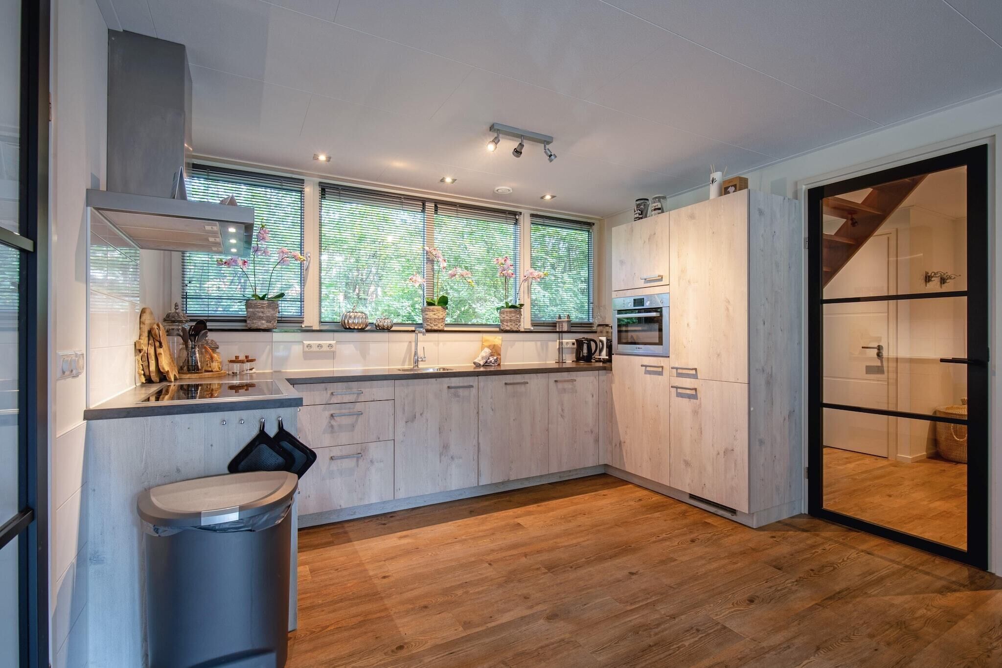 Een moderne keuken met houten kastjes, een inbouwoven en een groot raam met planten.