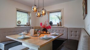 A dining area with a wooden table, cushioned seating, pendant lights, and decorative items. - Lovely villa on the edge of the forest (Den Burg)