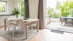 Eine moderne Küche mit weißen Schränken, einem Esstisch mit Stühlen und einem großen Fenster mit Vorhängen.