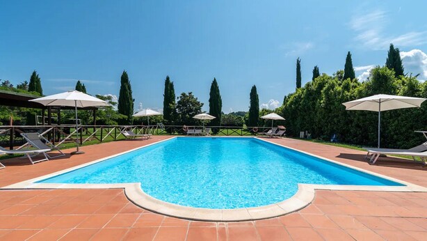 Et rektangulært pool med fliseterrasse, omgivet af liggestole og parasoller.