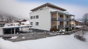 A modern multi-story building with a flat roof, a covered parking area, and a snow-covered landscape. - Modern apartment in Neukirchen (Neukirchen am Großvenediger)
