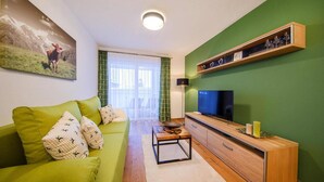 A living room with a green sofa, a TV, a wooden coffee table, and a green wall. - Modern apartment in Neukirchen (Neukirchen am Großvenediger)