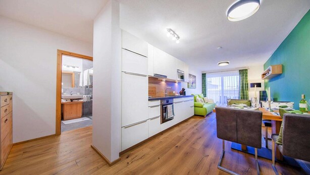 A modern kitchen with white cabinets, a wooden countertop, and a dining area with a green chair and table. - Modern apartment in Neukirchen (Neukirchen am Großvenediger)
