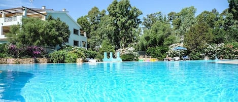 A clear blue swimming pool with lounge chairs and a white building in the background.