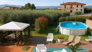 A backyard with a swimming pool, lounge chairs, a covered patio, and a view of a mountain.