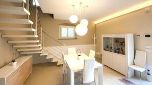 A modern interior with a staircase, dining area, and a cabinet with glass doors.