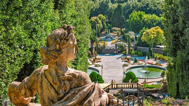 A large outdoor sculpture in a garden setting with a fountain and neatly trimmed hedges.