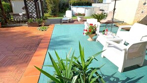 A pool area with lounge chairs, a covered seating area, and potted plants.
