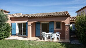 Una casa con un patio, un'area pranzo con sedie bianche e un tavolo, e una porta blu.
