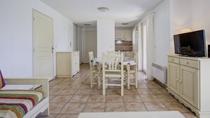 Una stanza piccola e ben illuminata con un tavolo da pranzo e sedie, una TV su un mobile basso e un letto con copriletto a righe.