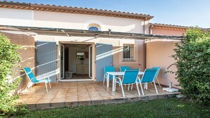 A patio with a table and chairs, a door leading to a room, and a small garden area. - P. Minervois J N°03 - Villa 3P6 (Homps)