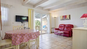 A dining area with a table and chairs, a television, a red sofa, and a lamp. - P. Minervois J N°03 - Villa 3P6 (Homps)