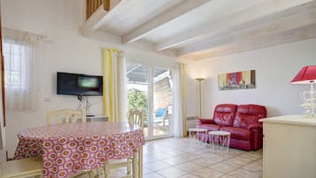 Un coin repas avec une table et des chaises, un téléviseur, un canapé rouge et une lampe.