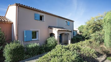 Une maison à deux étages, avec un toit recouvert de tuiles, une entrée principale dotée d’une porte bleue et un petit porche.