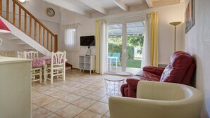 A living room with a wooden staircase, a dining table with chairs, a red sofa, and a TV on a stand. - P. Minervois J N°03 - Villa 3P6 (Homps)