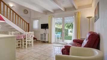 Un salon avec un escalier en bois, une table à manger avec des chaises, un canapé rouge et un téléviseur posé sur un meuble.