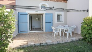 Um pátio com mesa e cadeiras, uma porta azul e um pequeno quarto com janela.