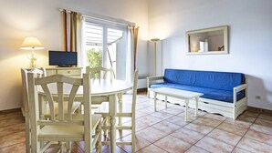 Quarto com uma mesa de jantar, cadeiras, um sofá azul, uma televisão e uma janela com cortinas.