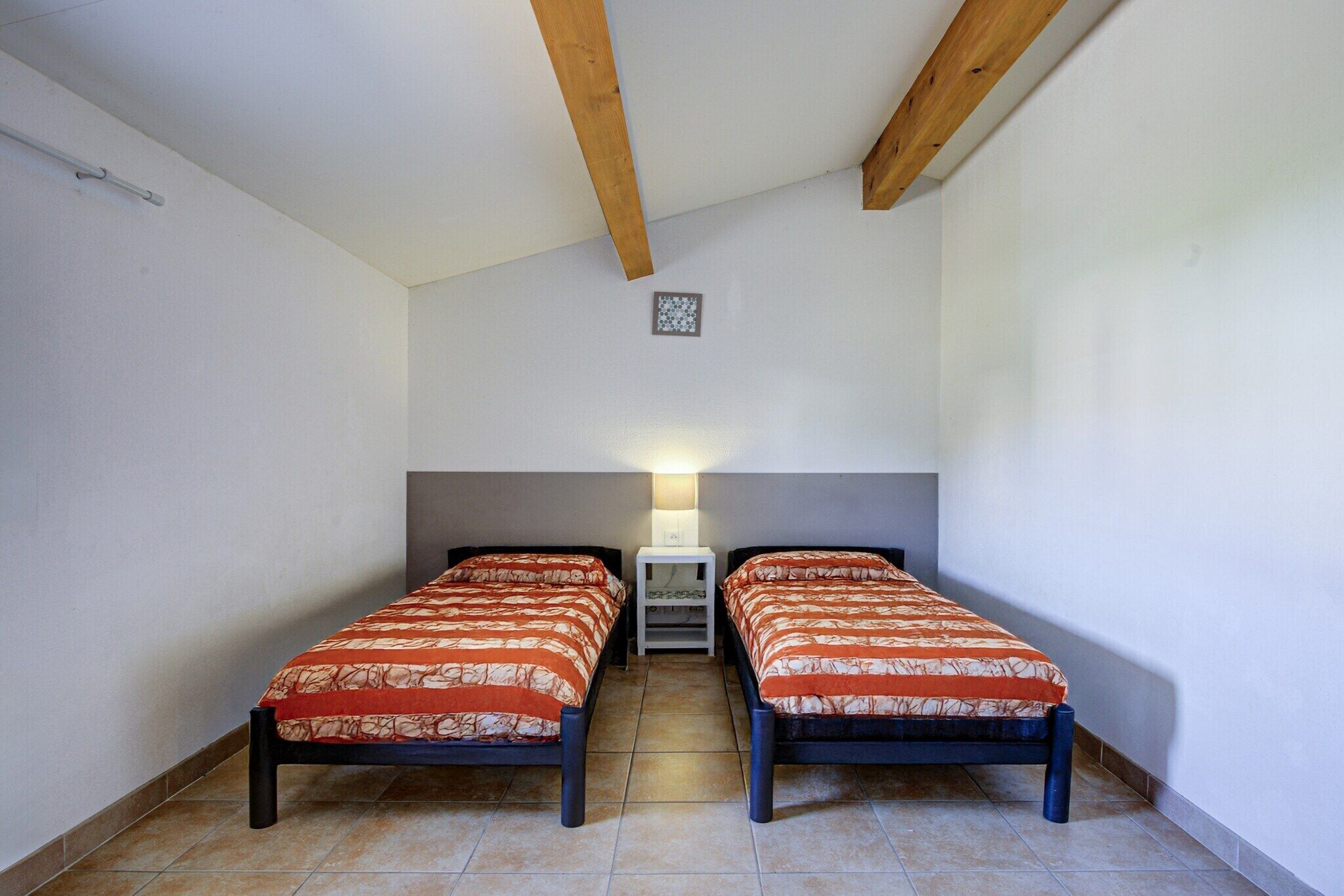 Une petite pièce simple, avec deux lits simples, une petite table et une lampe.
