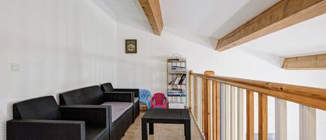 Ein Balkon mit Korbmöbeln, einem kleinen Tisch und einem Bücherregal.