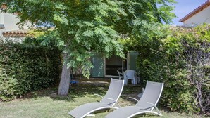 Two outdoor lounge chairs under a tree in a garden area with a building in the background. - Family Villa Near Lac de Jouarres (Homps)