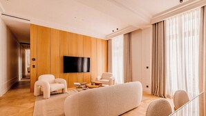 Un salon moderne doté d’un grand téléviseur à écran plat, d’un canapé, de deux fauteuils et d’un mur recouvert de panneaux en bois.