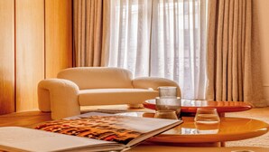 Un salon chaleureux avec un fauteuil beige, une table basse sur laquelle reposent des verres et un magazine posé sur le sol.