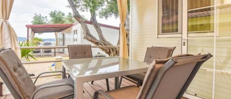 A covered outdoor seating area with a glass table and chairs, overlooking a backyard with a patio and a house.