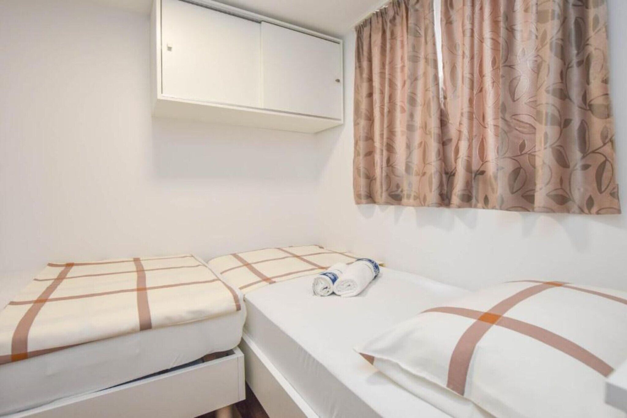 A small, clean room with two beds, a wardrobe, and a window with curtains.