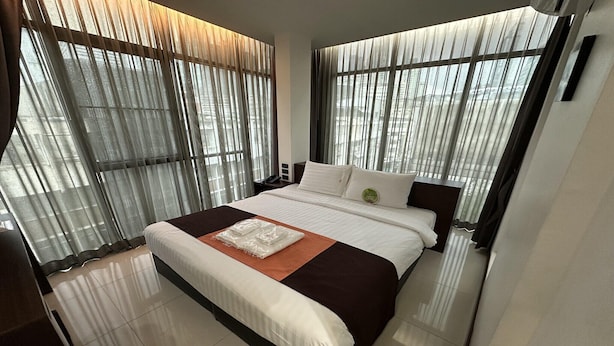 Habitación de hotel moderna con una cama grande, una mesita de noche y vistas a través de cortinas translúcidas.