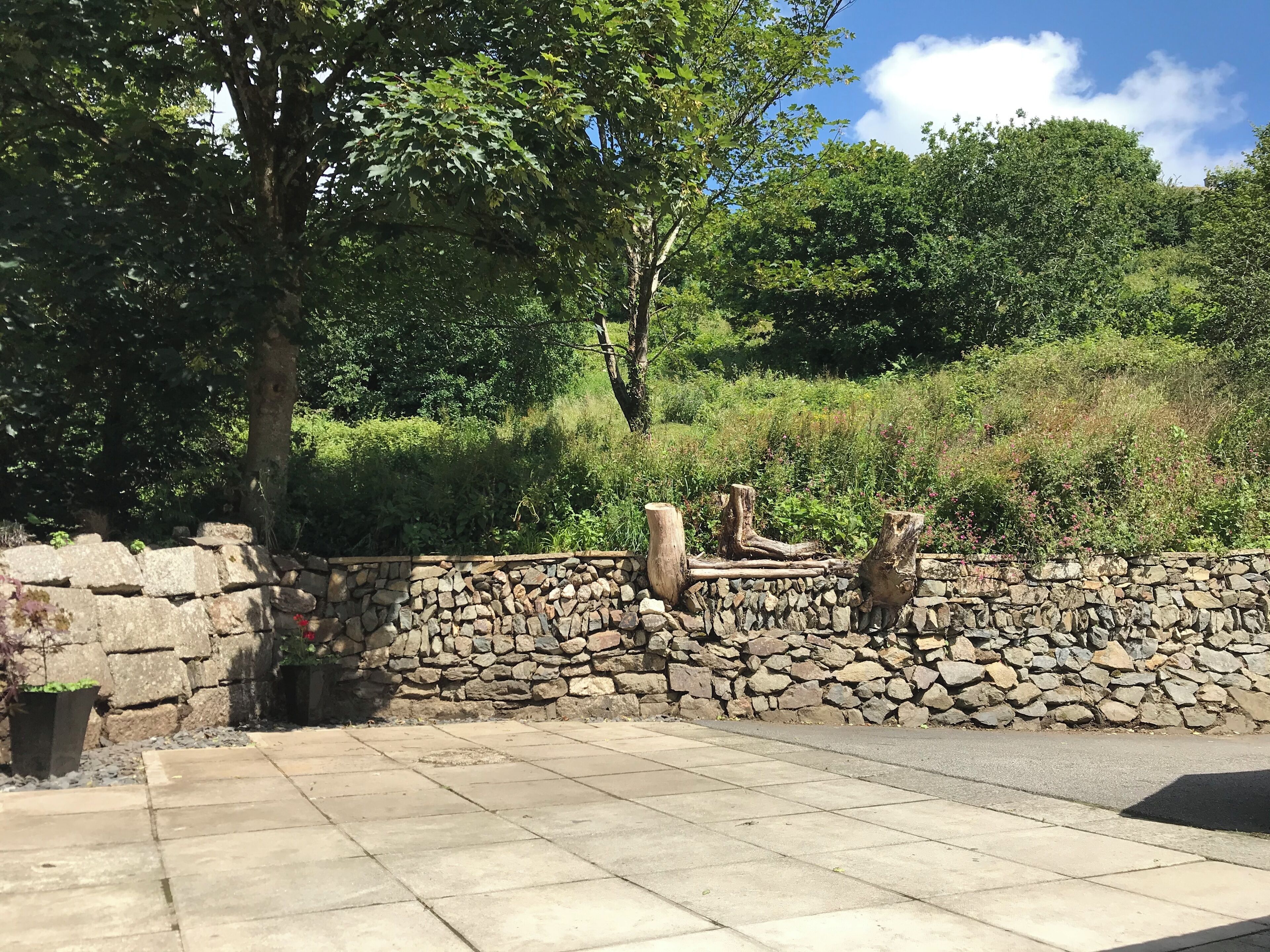 A stone wall with a stone pathway leading to a grassy area with trees.