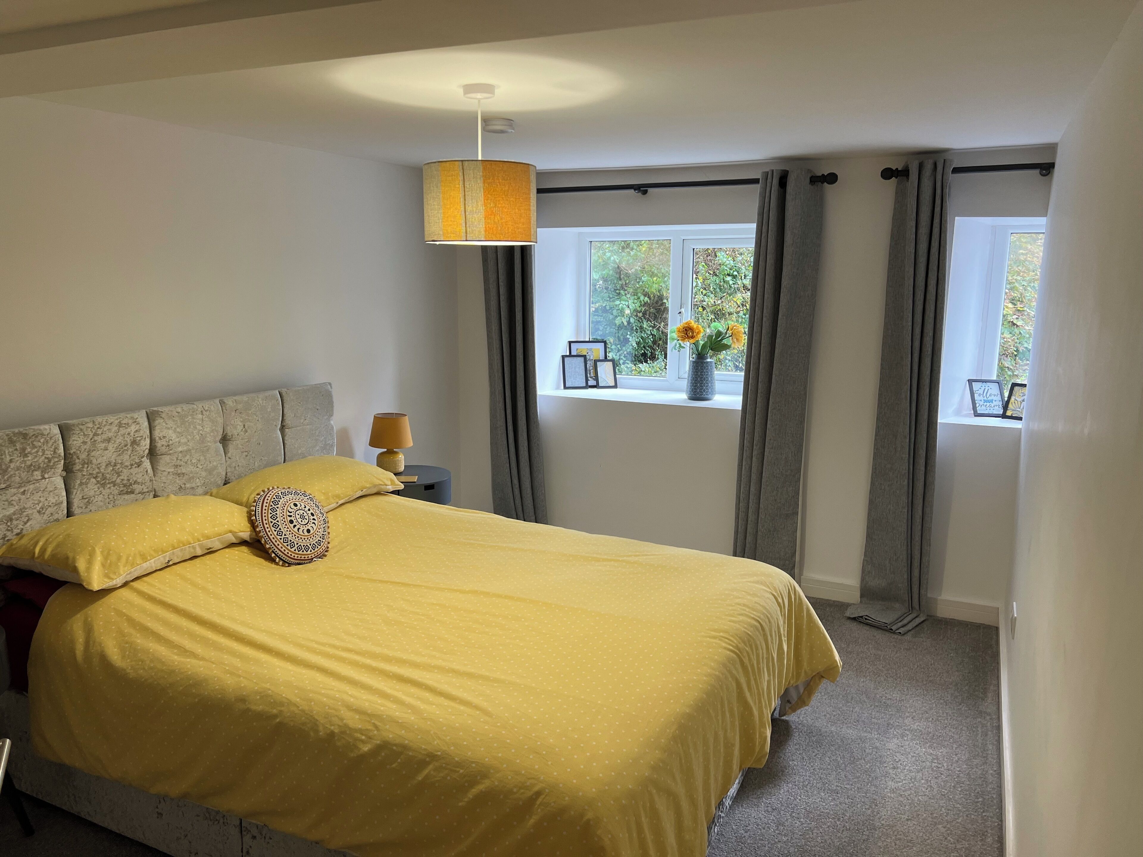 Una camera da letto con un letto grande, un comodino con una lampada, una finestra con tende e vista sul verde circostante.