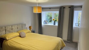 Een slaapkamer met een groot bed, een nachtkastje met lamp, een raam met gordijnen en uitzicht op groen.