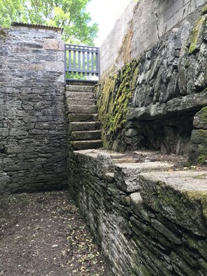 Un escalier en pierre mène à une porte en bois, l’ensemble étant entouré de murs de pierre recouverts de mousse.